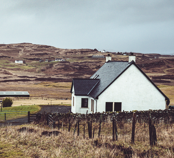 White house in a green field with a wall running through the land.